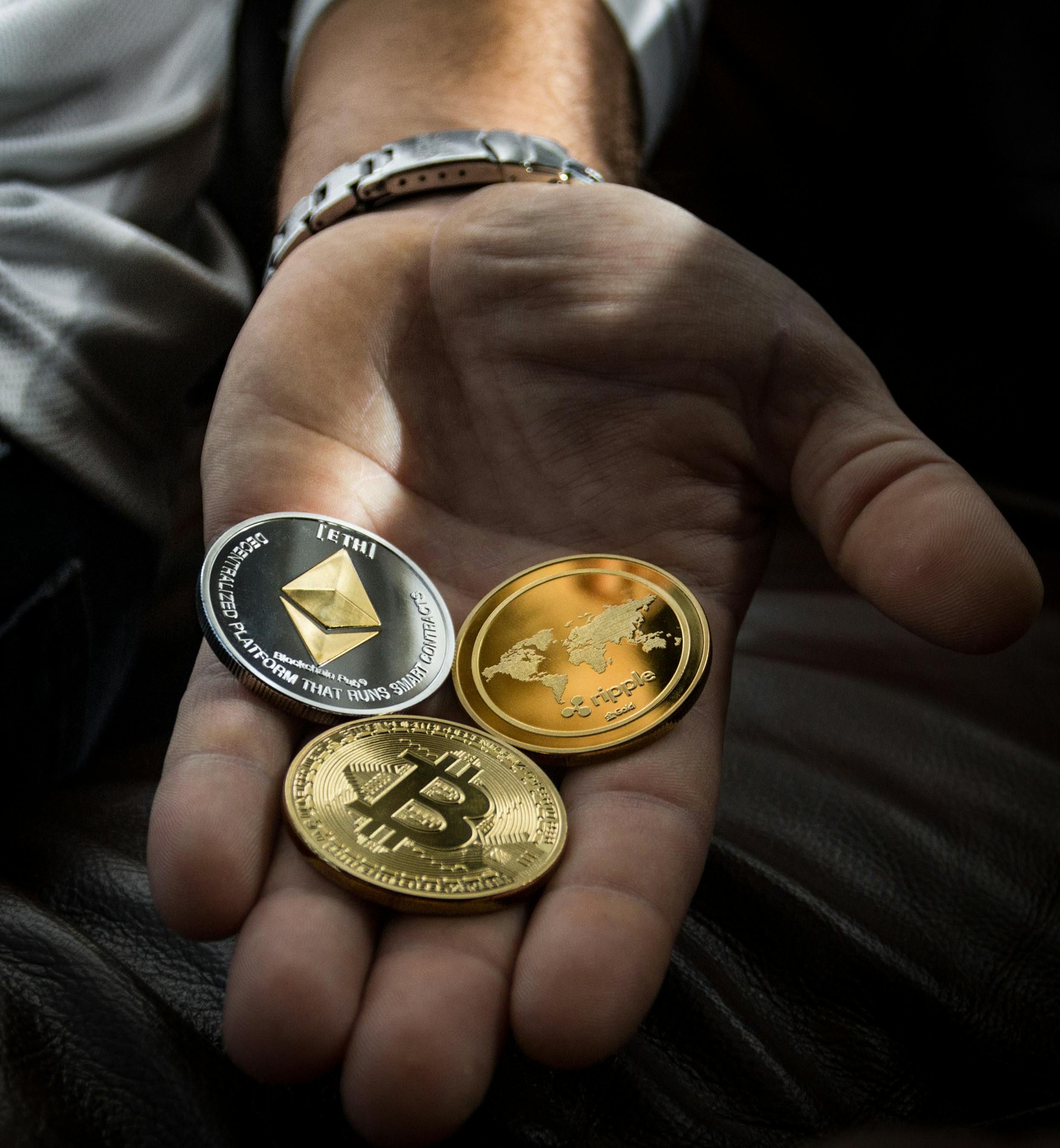 Mano con tres criptomonedas: moneda de Bitcoin, Ethereum y Ripple, simbólicas de activos digitales e inversiones cripto.