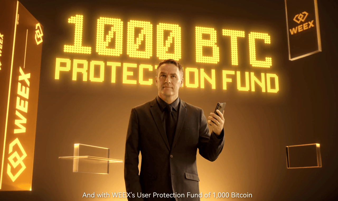 Michael Owen de pie en una habitación dorada con un smartphone en la mano. Detrás de él, las palabras “1000 BTC Protection Fund” brillan en grandes letras amarillas, rodeadas de logotipos de WEEX.